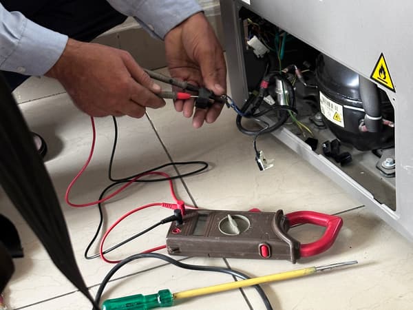 An appliance technician checking and replacing a fridge’s compressor